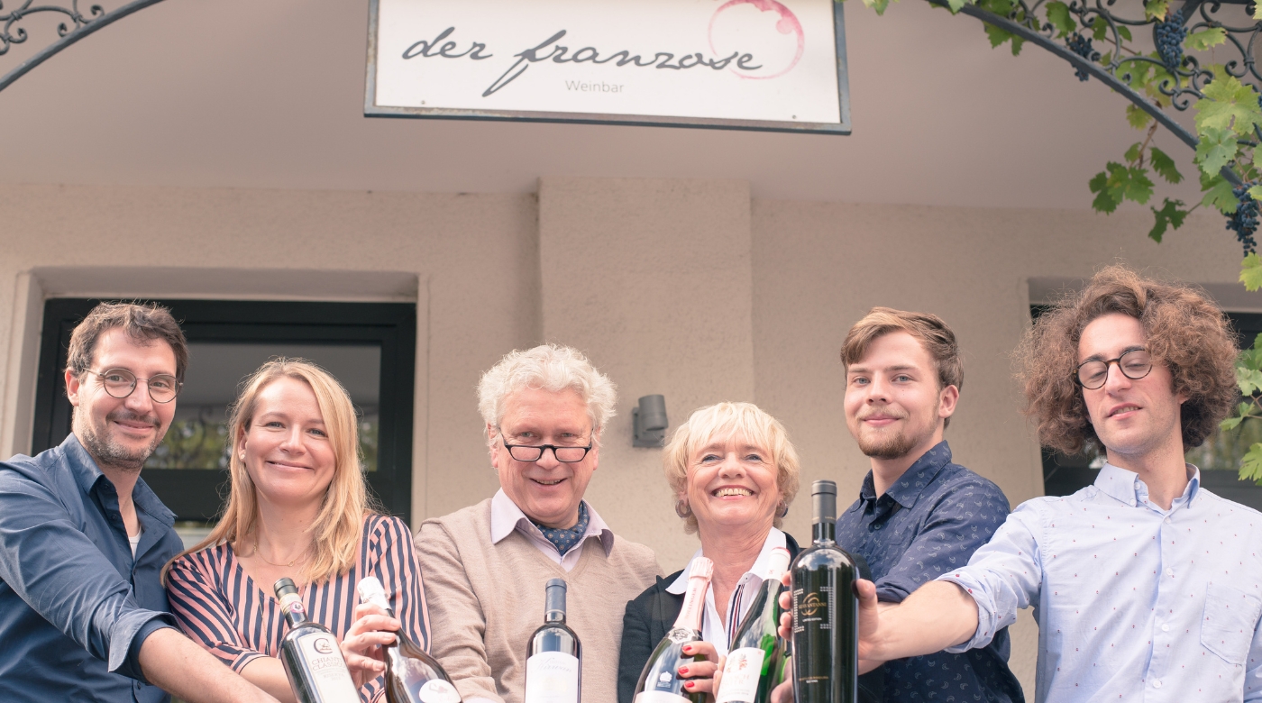 Sechs Personen vor Weinbar „der franzose“ präsentieren verschiedene Weinflaschen.