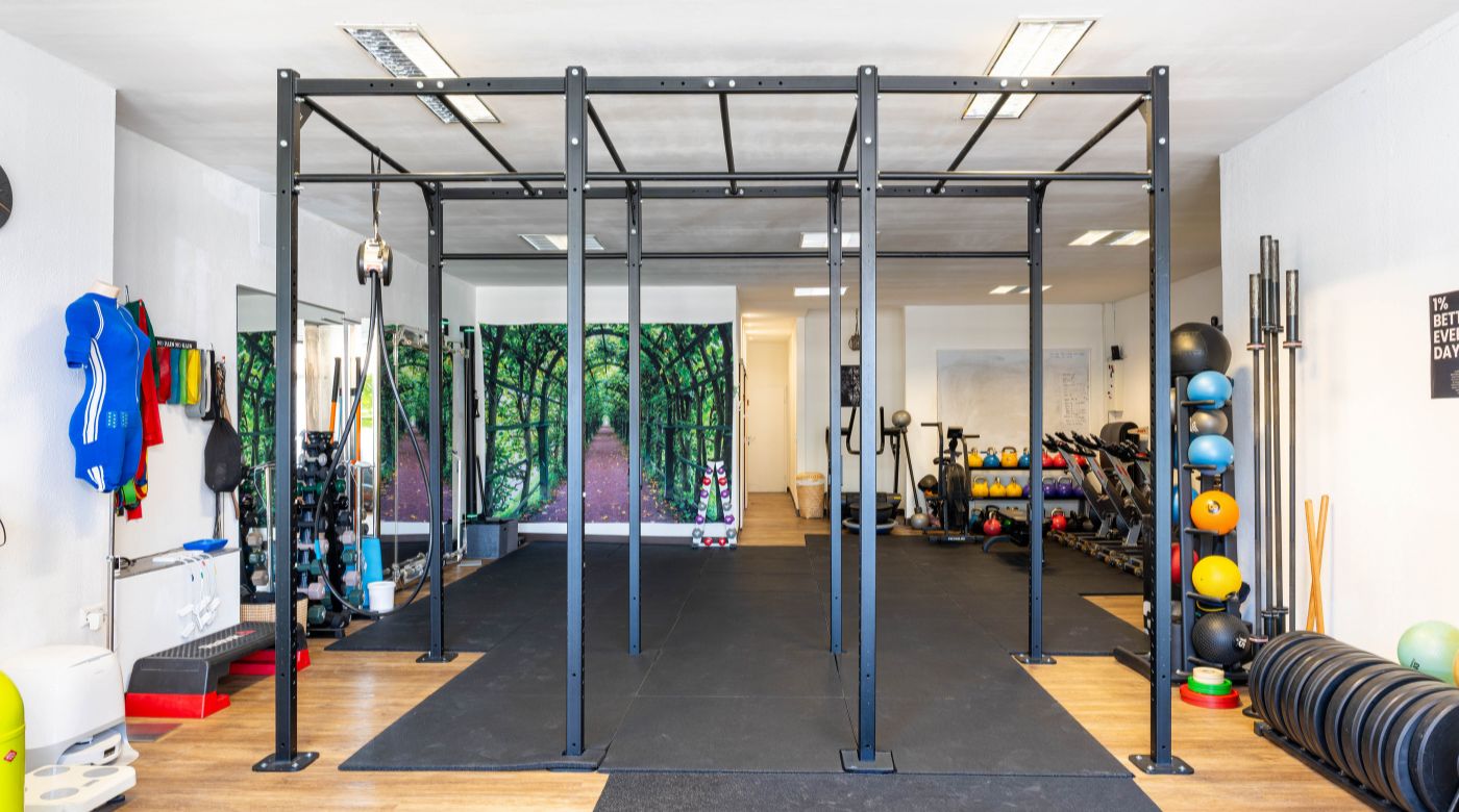 Heller Fitnessraum mit schwarzem Trainingsgerüst und Sportgeräten.