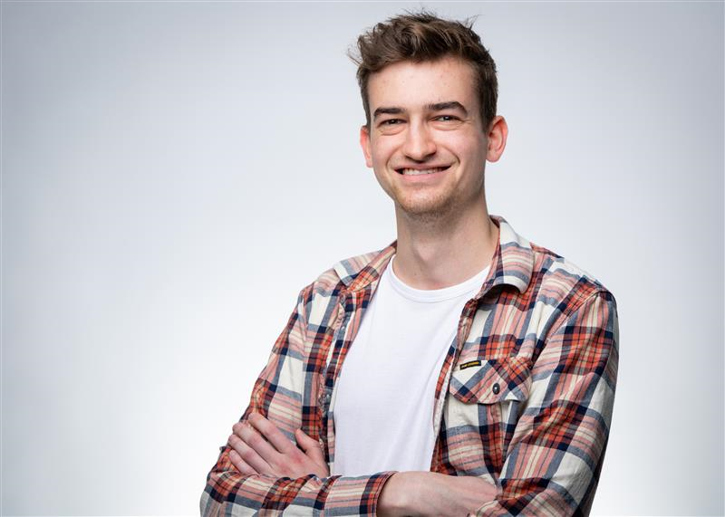 Junger Mann mit kariertem Hemd lächelt in die Kamera