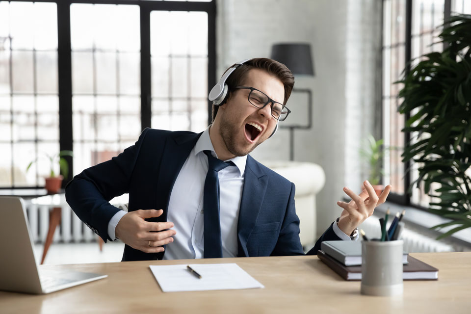 Foto eines jungen Mannes im Büro, der mit Kopfhörer Musik hört und dazu Luftgitarre spielt. (Foto: fizkes/Shutterstock)