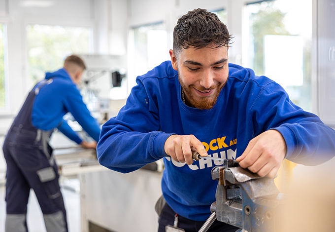 Auszubildender arbeitet an Schraubstock in Werkstatt