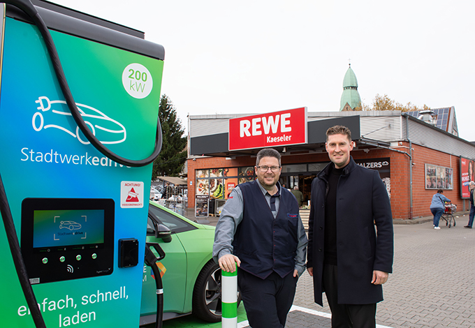 v.l. André Kaeseler und Jannis Bär an den neuen HPC-Ladestationen auf dem REWE-Parkplatz in Bochum-Gerthe