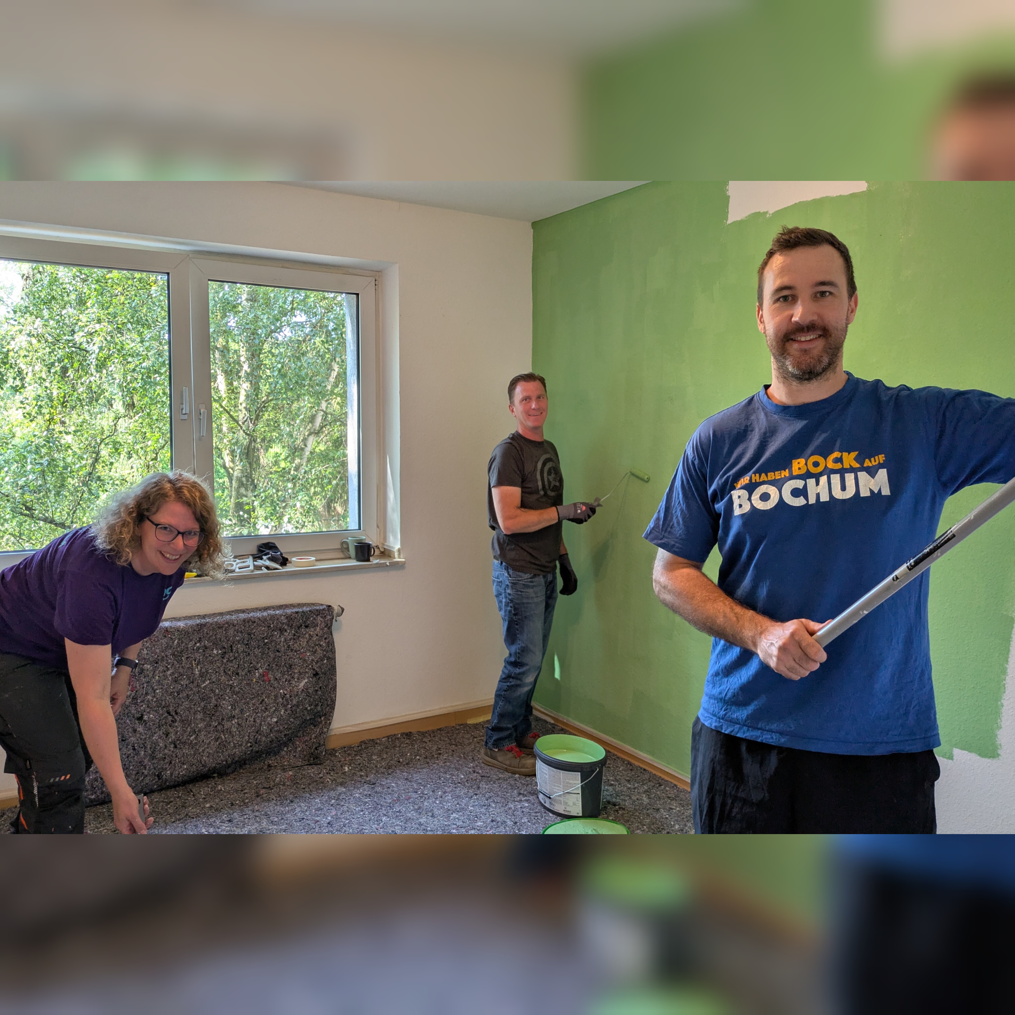Drei Personen streichen eine Wand in einem Raum mit grünem Anstrich