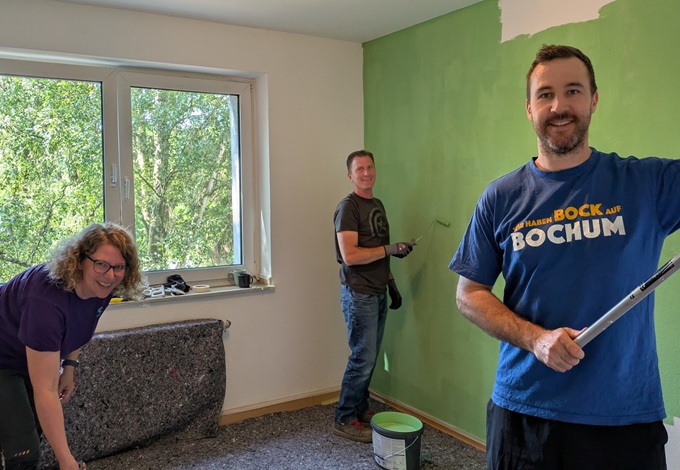 Drei Personen streichen eine Wand in einem Raum mit grünem Anstrich