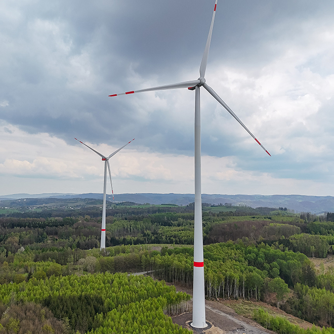 Zwei Windräder in einer grünen Landschaft unter bewölktem Himmel