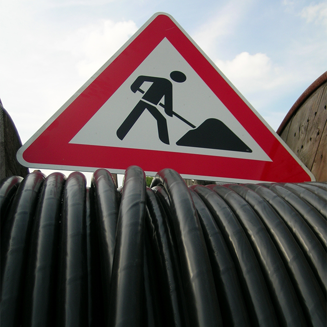 Verkehrsschild für Bauarbeiten über Kabelrollen, die auf einem Baustellenfahrzeug geladen ist.