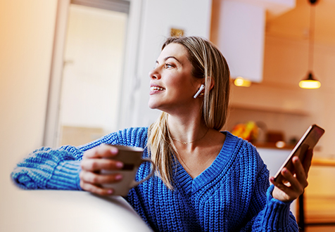 Junge Frau mit blauem Pullover hält Tasse und Smartphone
