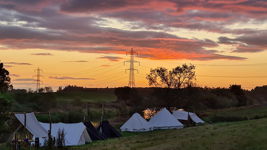 Zelte bei Sonnenuntergang mit Stromleitungen im Hintergrund