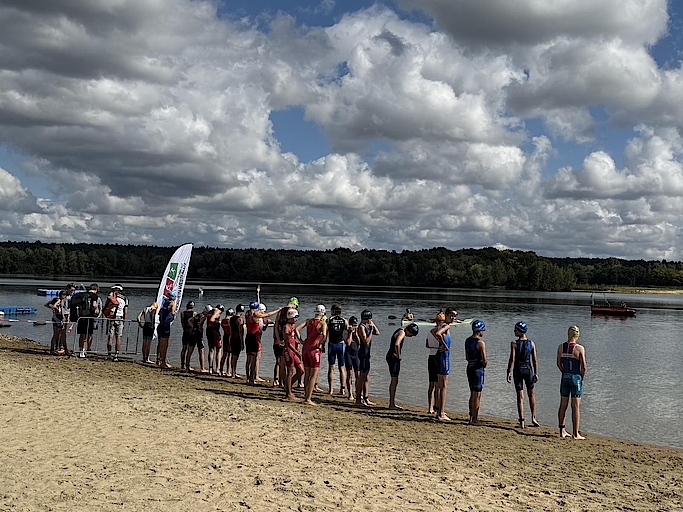 Sportler am Seeufer vor dem Start eines Schwimmwettbewerbs