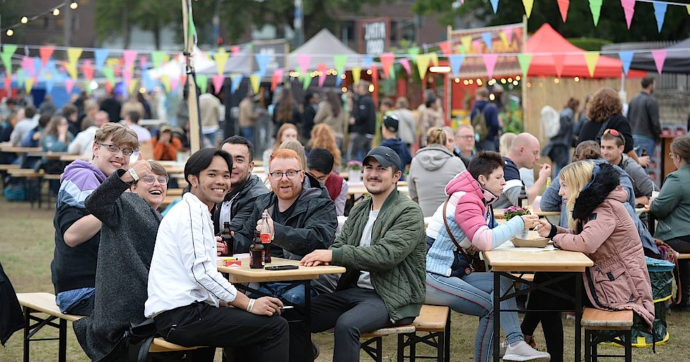 Menschen sitzen bei einer Outdoor-Veranstaltung an Tischen