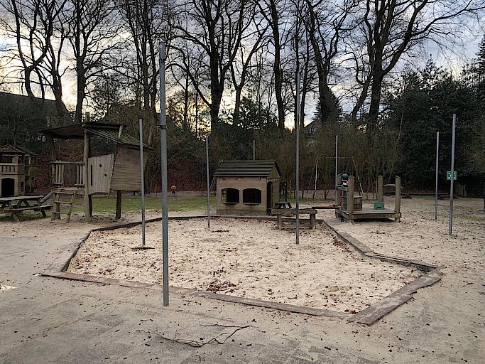 Spielplatz mit Sandfläche und Holzhäusern im Park