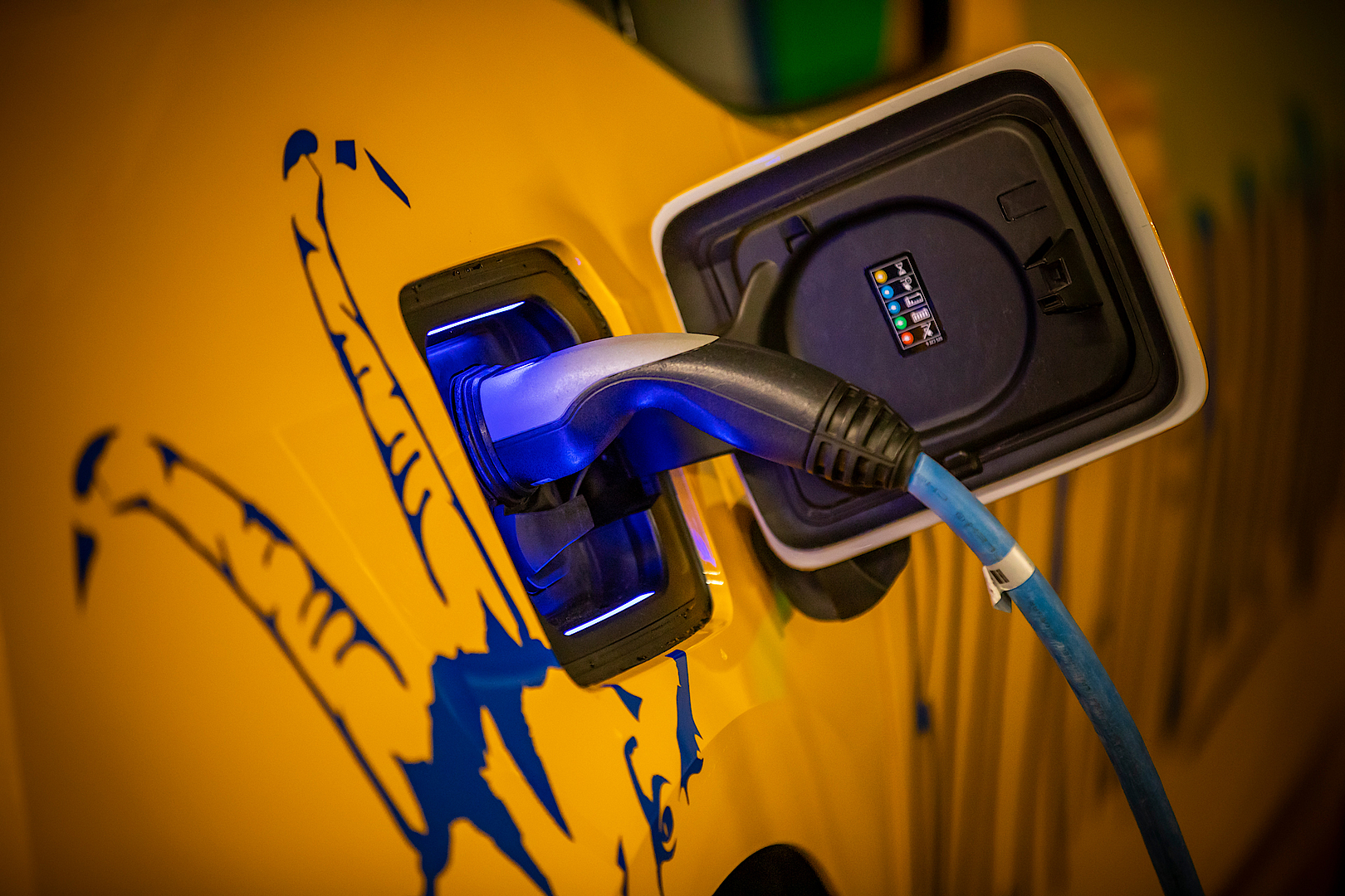 Nahaufnahme eines Ladekabels, das an ein Elektrofahrzeug angeschlossen ist, mit sichtbarem Firmenlogo.