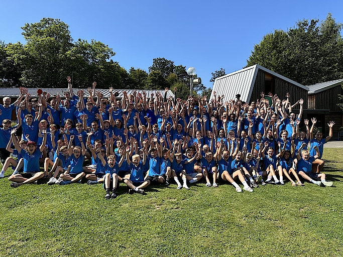 Große Gruppe von Kindern und Erwachsenen hebt die Hände im Freien