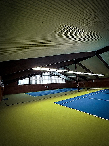 Blick auf eine leere Tennishalle mit blauen Plätzen