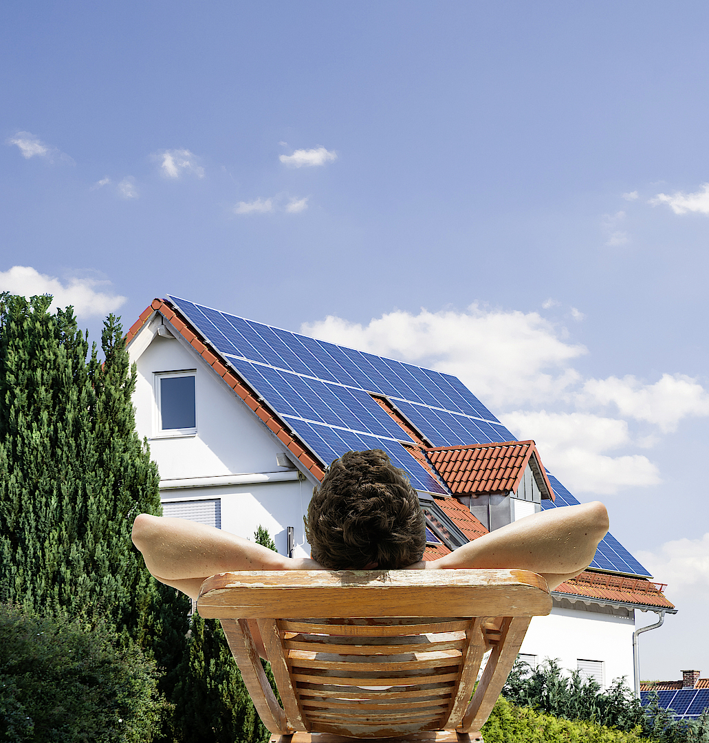 Mann entspannt sich vor Haus mit Solarpaneelen auf dem Dach