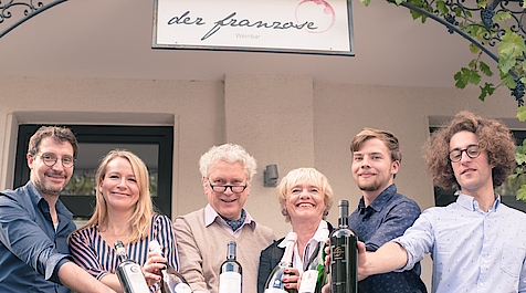 Sechs Personen vor Weinbar „der franzose“ präsentieren verschiedene Weinflaschen.