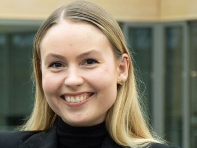 Porträt einer lächelnden jungen Frau in einem schwarzen Blazer, die in die Kamera schaut.