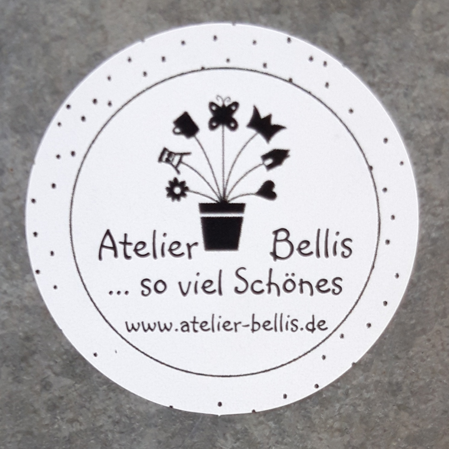 Rundes Logo von Atelier Bellis mit Blumentopf, Slogan "so viel Schönes" und Website.