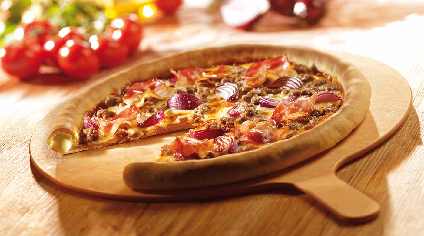 Pizza auf Holzbrett, belegt mit Speck, Hackfleisch, roten Zwiebeln und geschmolzenem Käse.