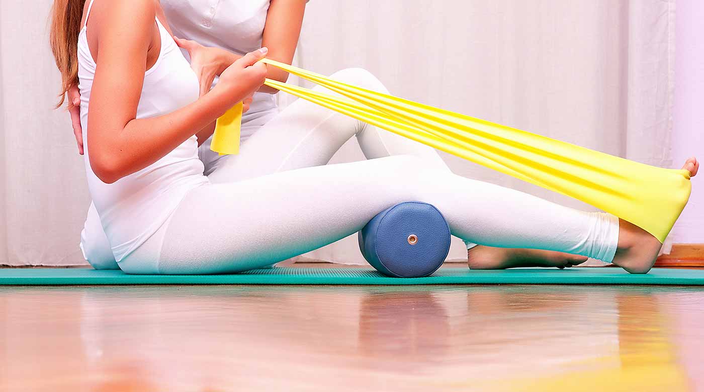 Frau trainiert mit gelbem Band und Schaumrolle auf einer Matte.