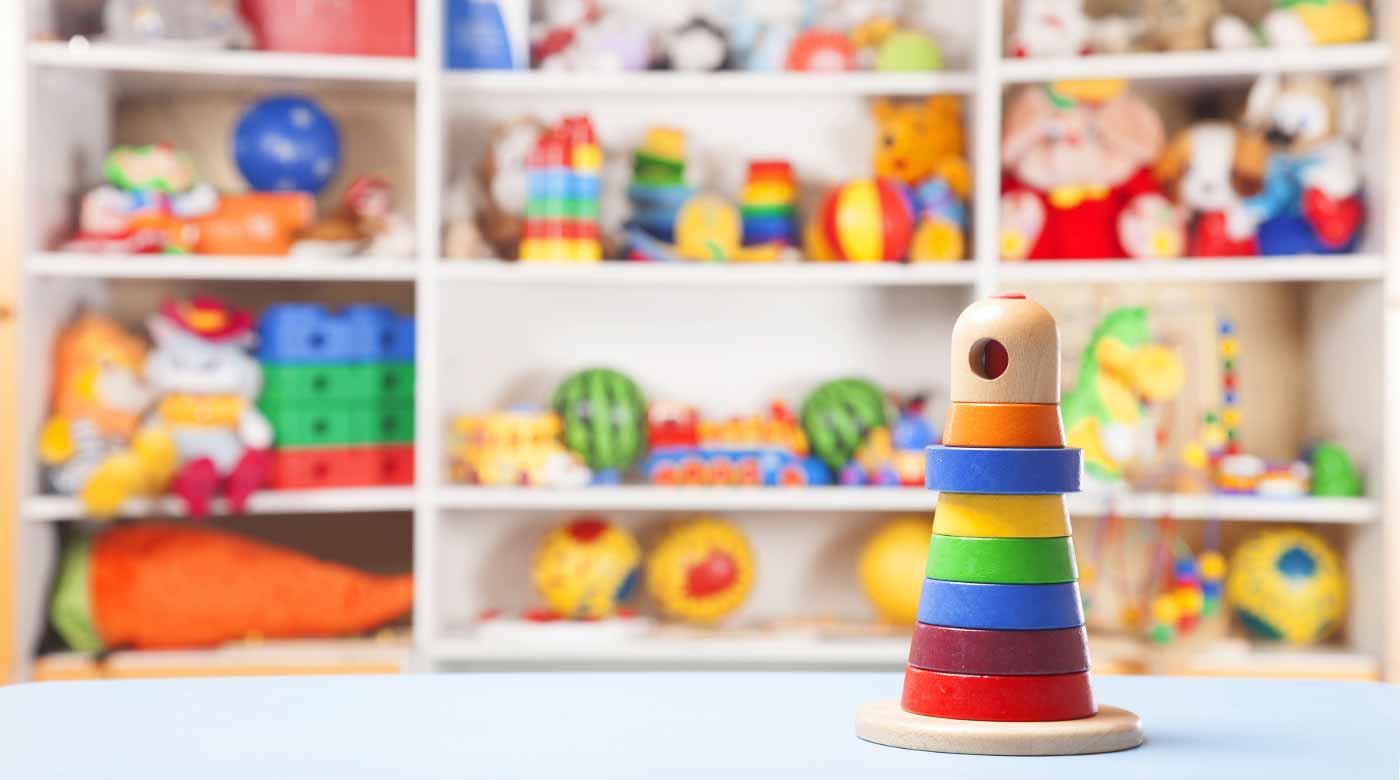 Bunter Stapelturm aus Holz vor einem Regal mit verschiedenen Spielzeugen im Hintergrund.