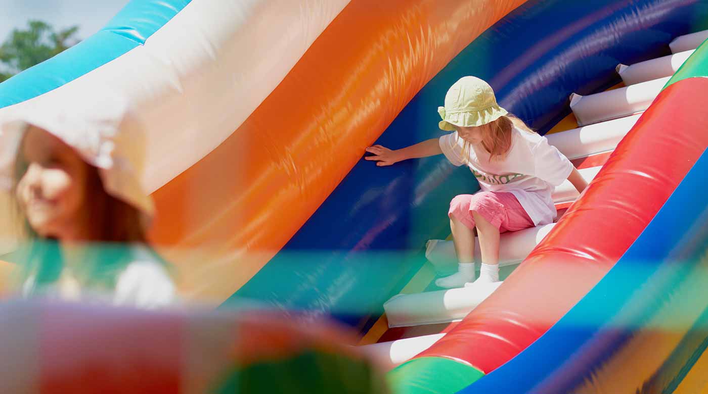 Kind rutscht auf einer bunten Hüpfburg mit orange-blauen und roten Elementen.