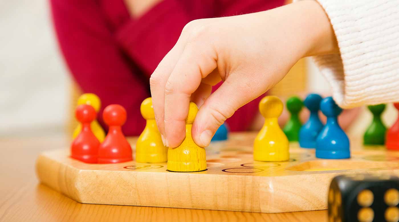 Hand bewegt gelbe Spielfigur auf einem Brettspiel mit bunten Figuren und Würfel.