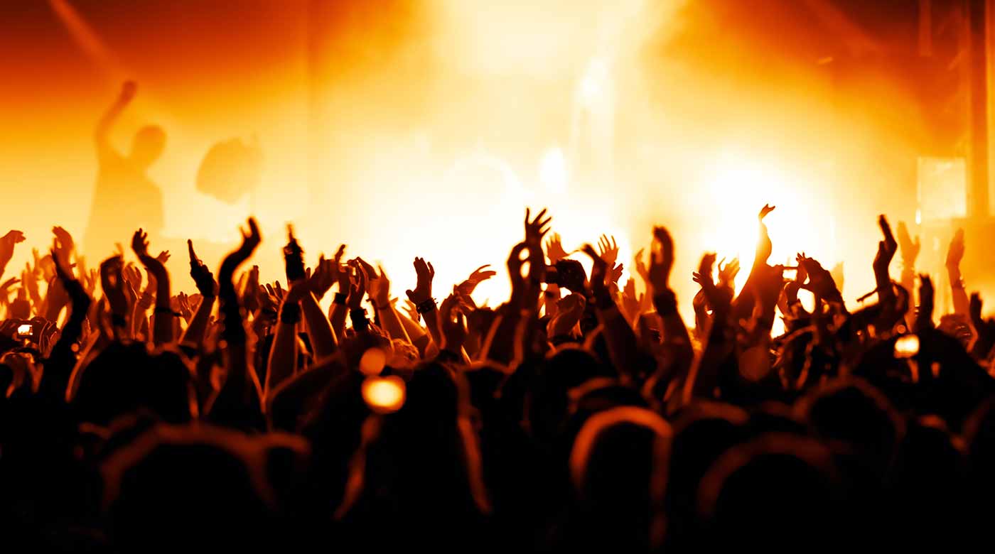 Jubelnde Menschenmenge bei einem Konzert in warmem, orangefarbenem Bühnenlicht.