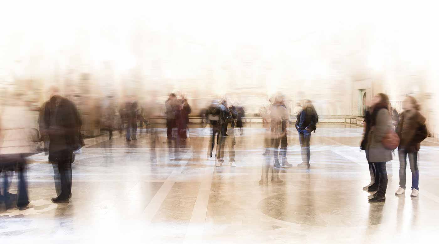 Menschen bewegen sich in einer hellen, verschwommenen Halle mit reflektierendem Boden.