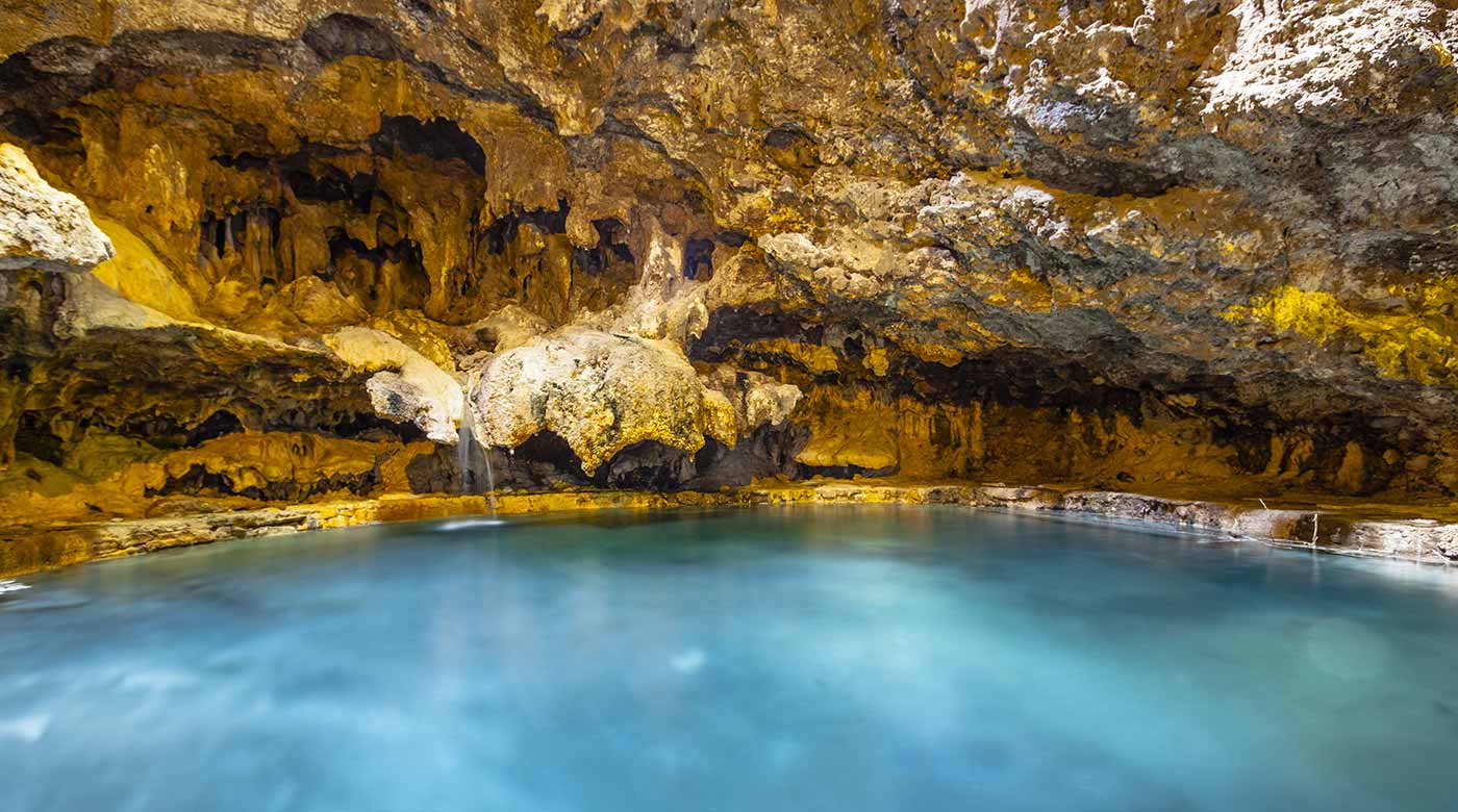 Beleuchtete Tropfsteinhöhle mit klarem, blauem Wasser und beeindruckenden Felsformationen.