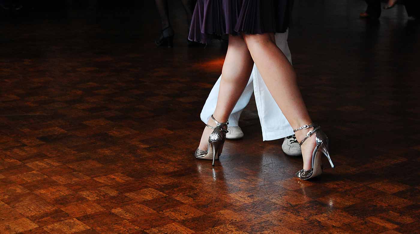 Tanzpaar auf Parkettboden, Fokus auf elegante Schuhe und Beinarbeit.