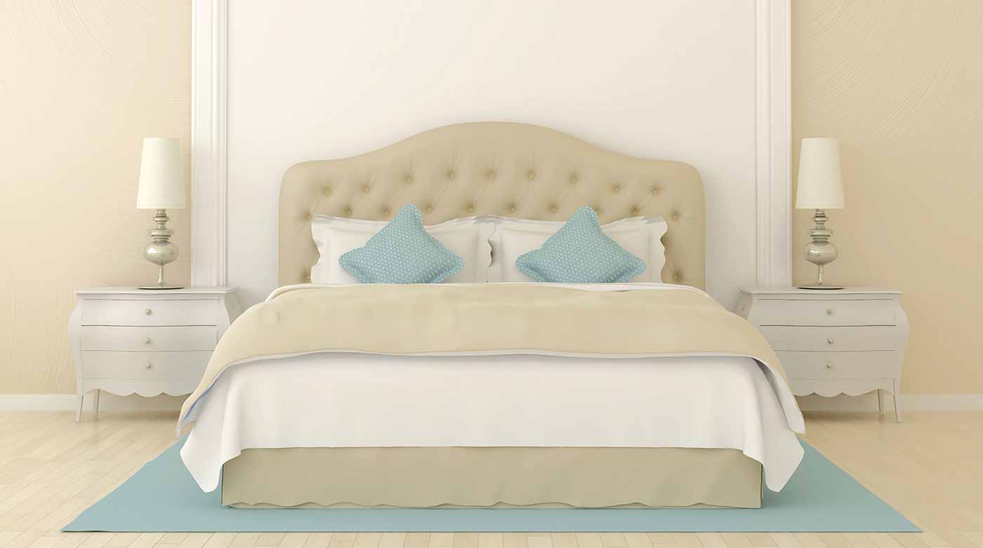 Elegantes Bett mit beigem Kopfteil, blauen Kissen, Nachttischen und Lampen.