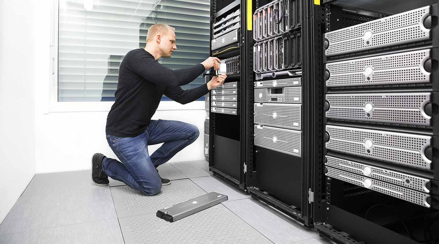 Techniker arbeitet an Server-Racks in einem hellen Raum mit Fenster und Jalousien.