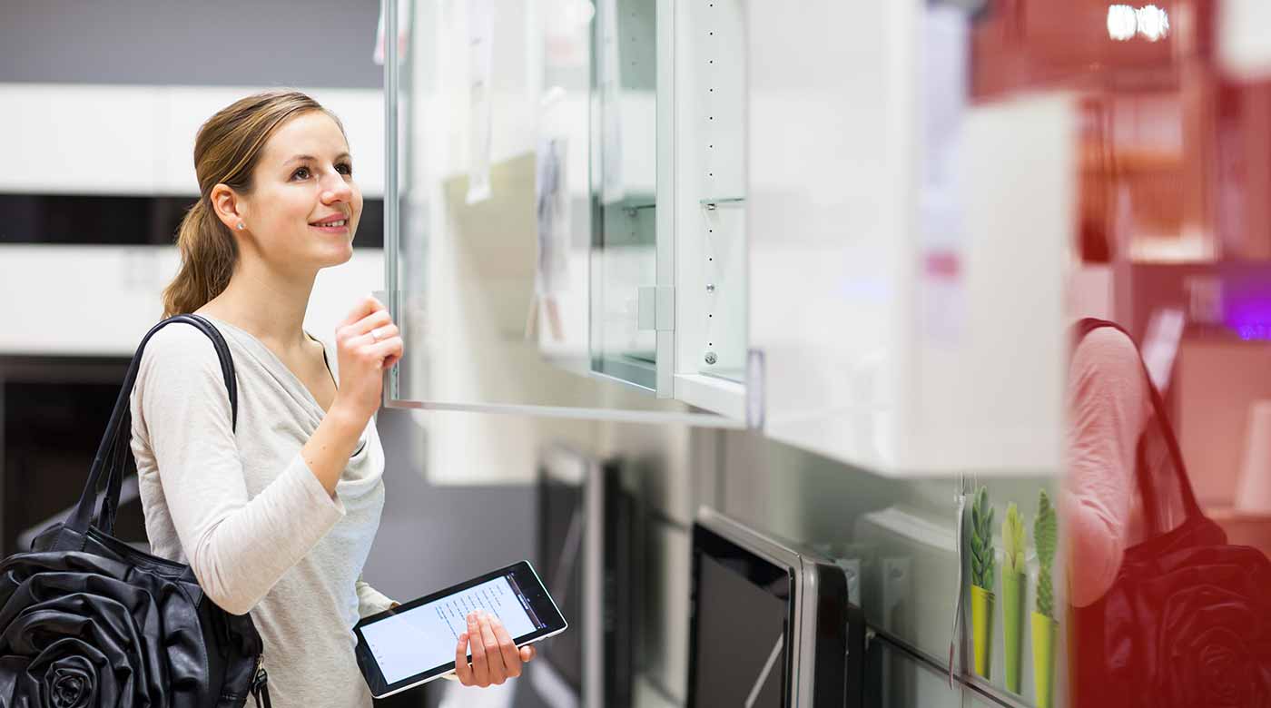 Kundin inspiziert moderne Kühlschränke in einer Ausstellung, Tablet in der Hand.