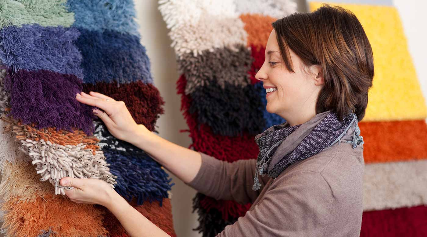 Person begutachtet bunte Teppichmuster mit unterschiedlichen Texturen in einer Ausstellung.
