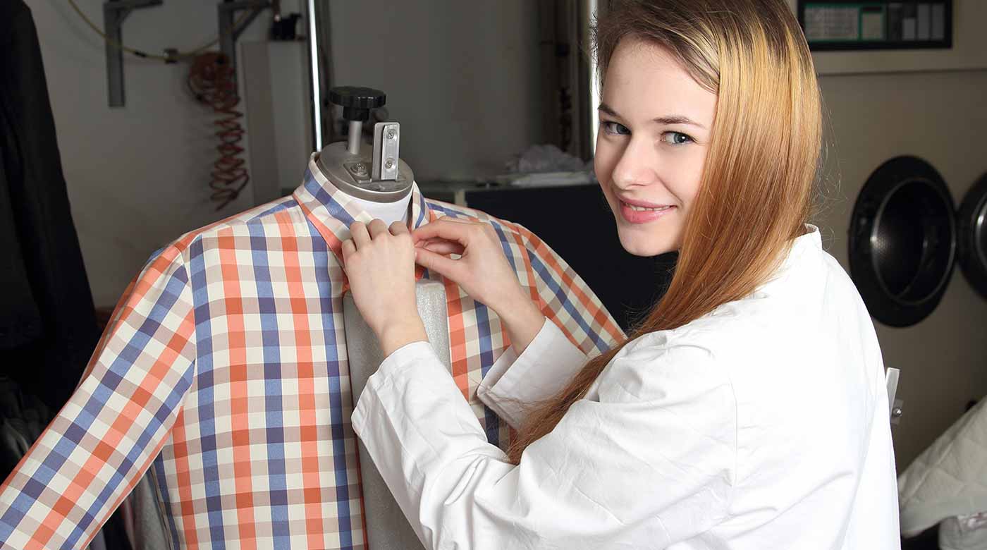 Person richtet ein kariertes Hemd auf einer Bügelpuppe in einer Wäscherei.