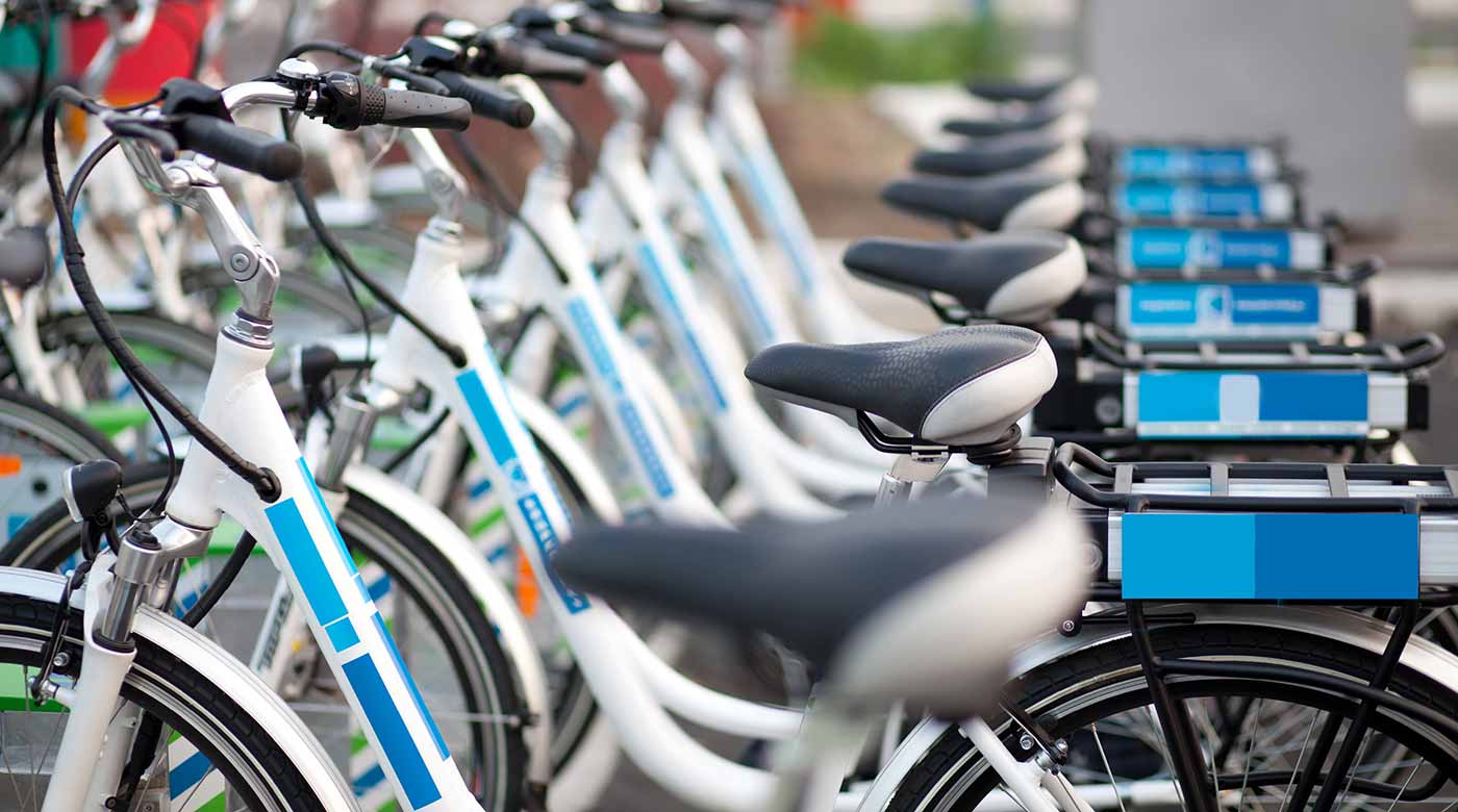 Reihe weißer Leihfahrräder mit blauen Akzenten, geparkt in einer Fahrradstation.