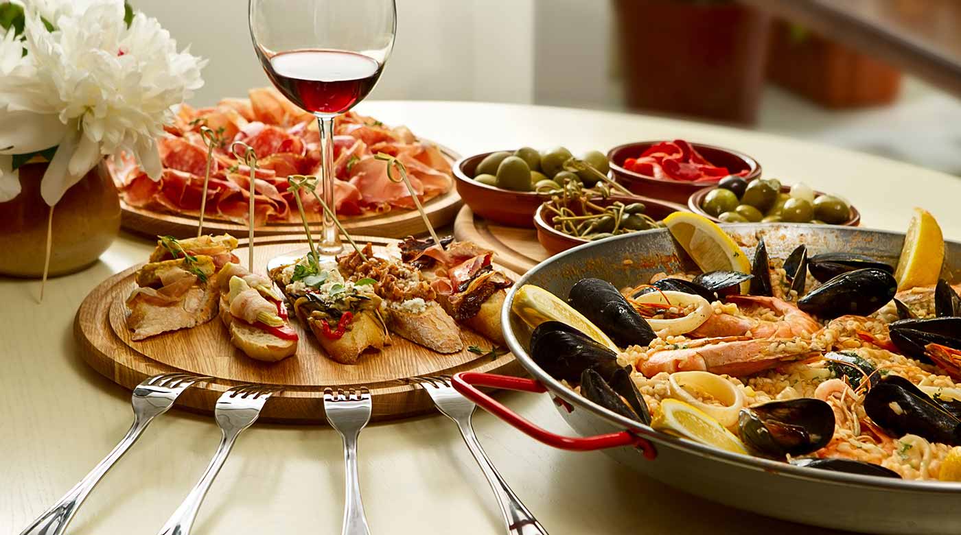 Mediterranes Essen mit Paella, Tapas, Oliven, Schinken und Rotwein auf einem gedeckten Tisch.