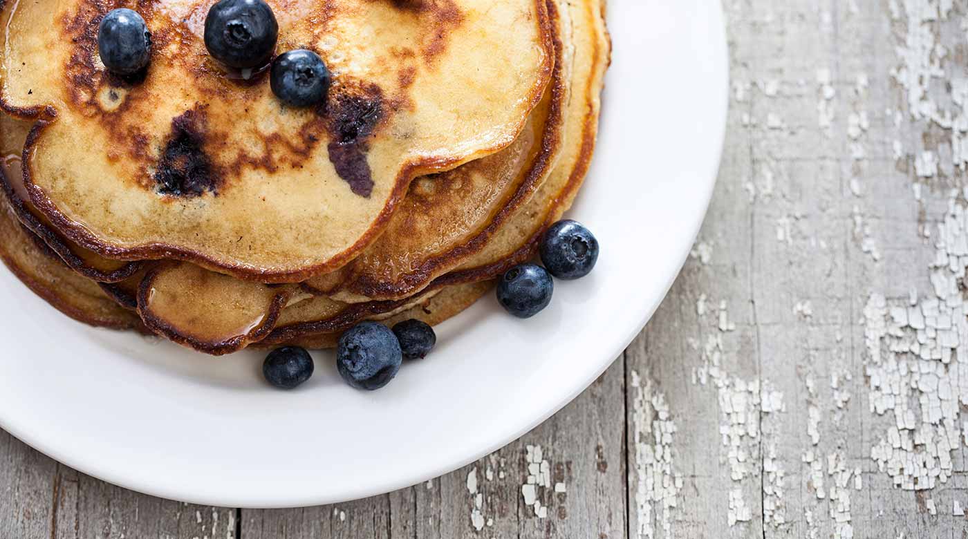 Stapel Pfannkuchen mit frischen Blaubeeren und Sirup auf einem weißen Teller.