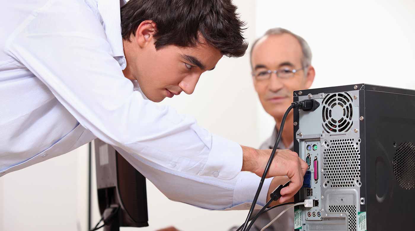 Mann schließt Kabel an der Rückseite eines Desktop-Computers in einem Büro an.