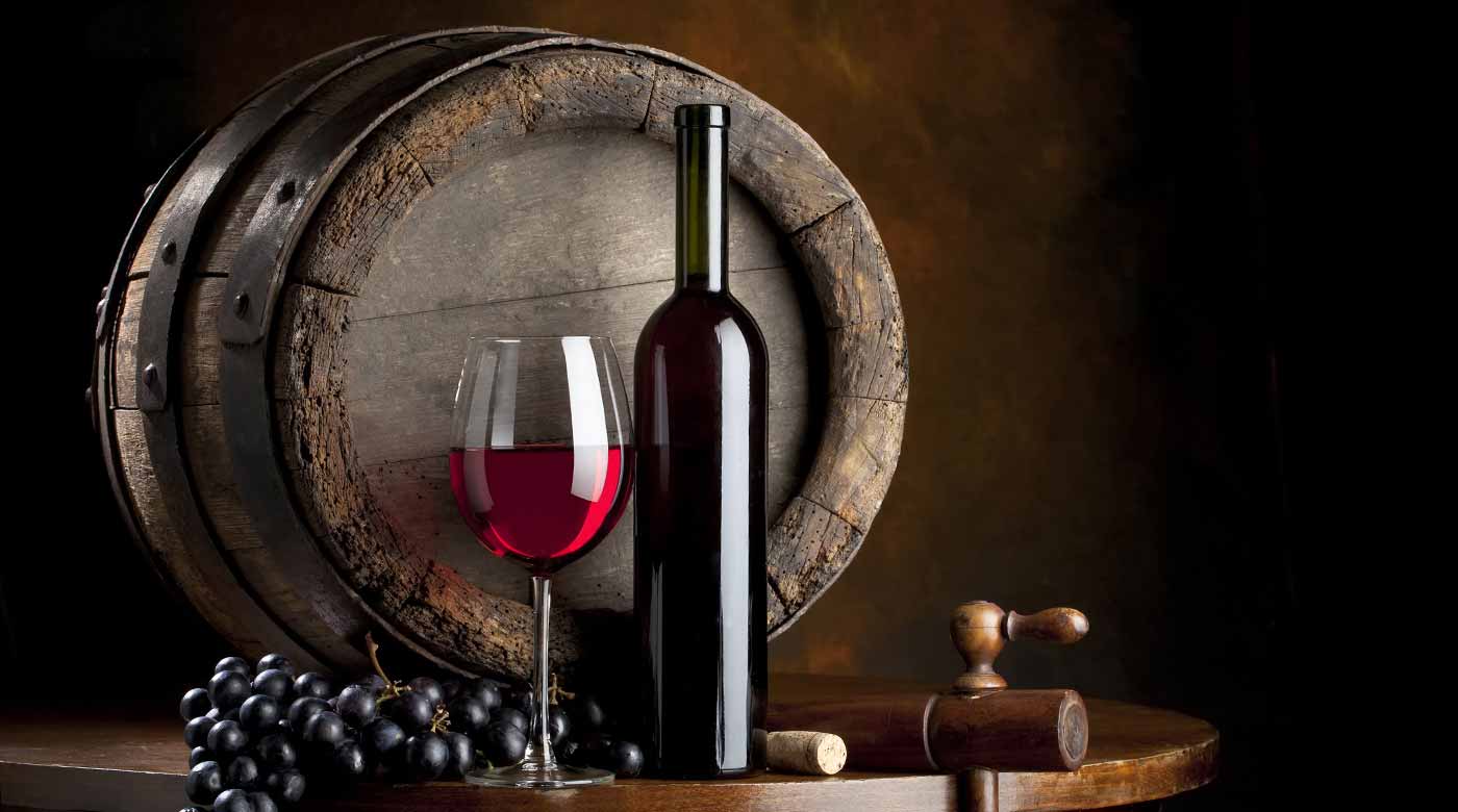 Weinflasche, Glas Rotwein, Trauben und altes Holzfass auf dunklem Hintergrund.