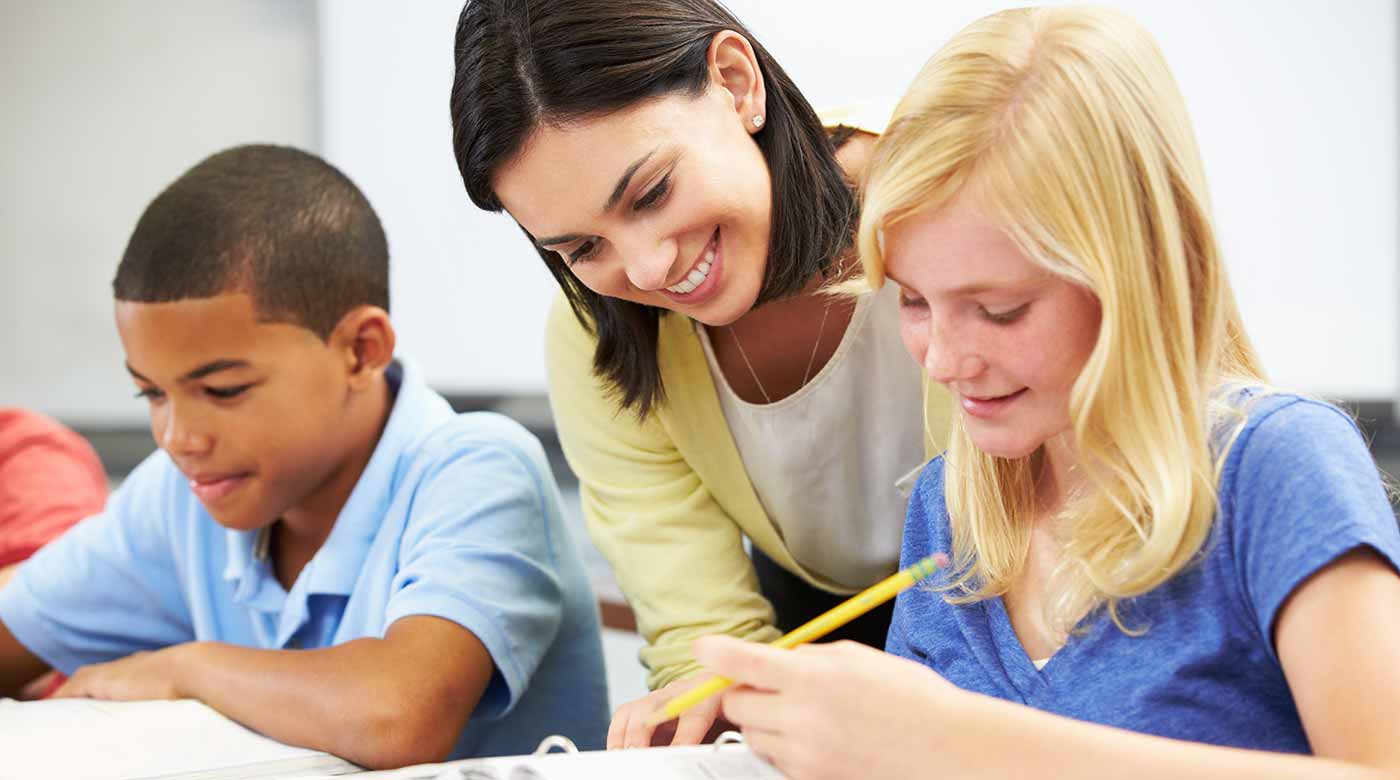 Lehrerin unterstützt zwei Kinder beim Lernen in einem Klassenzimmer mit Schreibmaterial.
