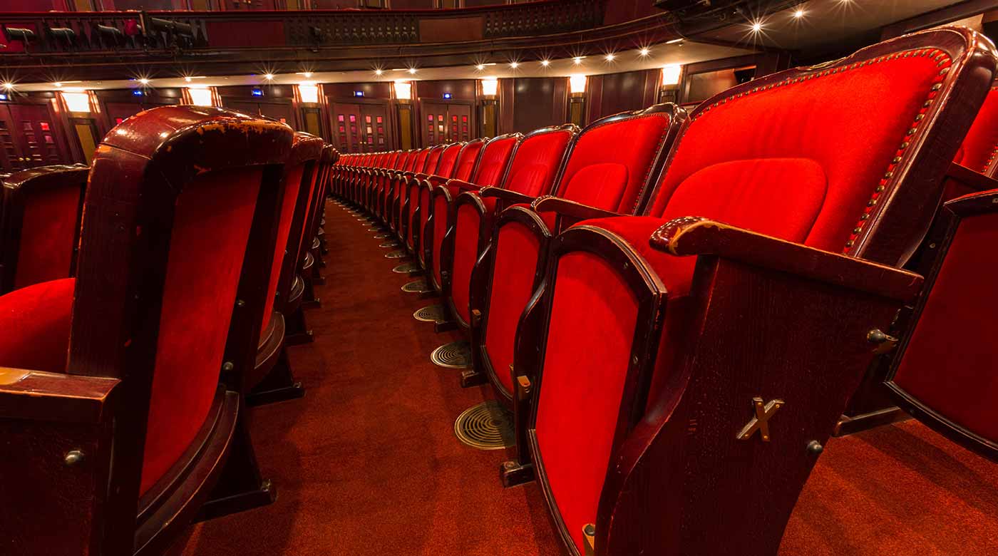 Reihe roter Theatersitze in einem historischen Saal mit warmem Licht.