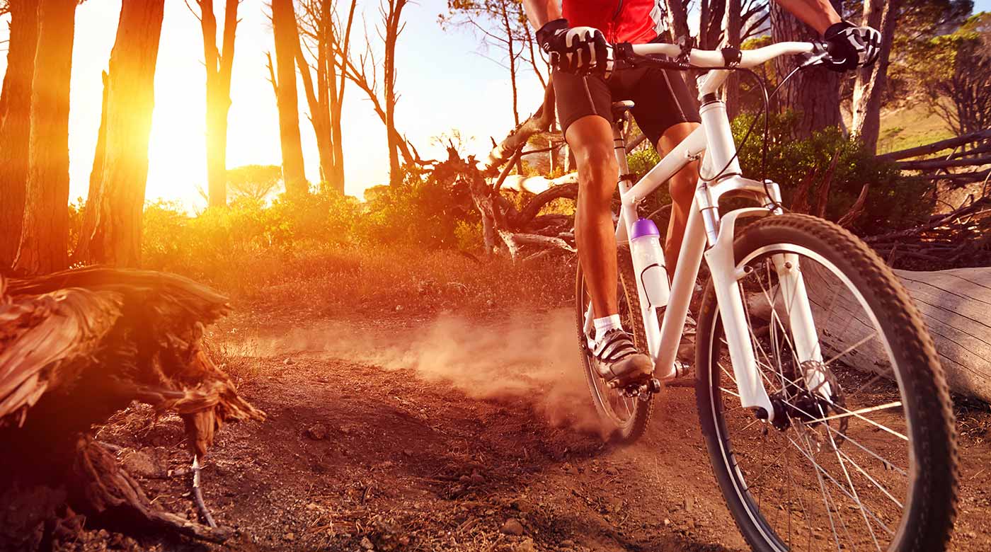 Mountainbiker fährt dynamisch durch Waldweg bei Sonnenuntergang, aufwirbelnder Staub.