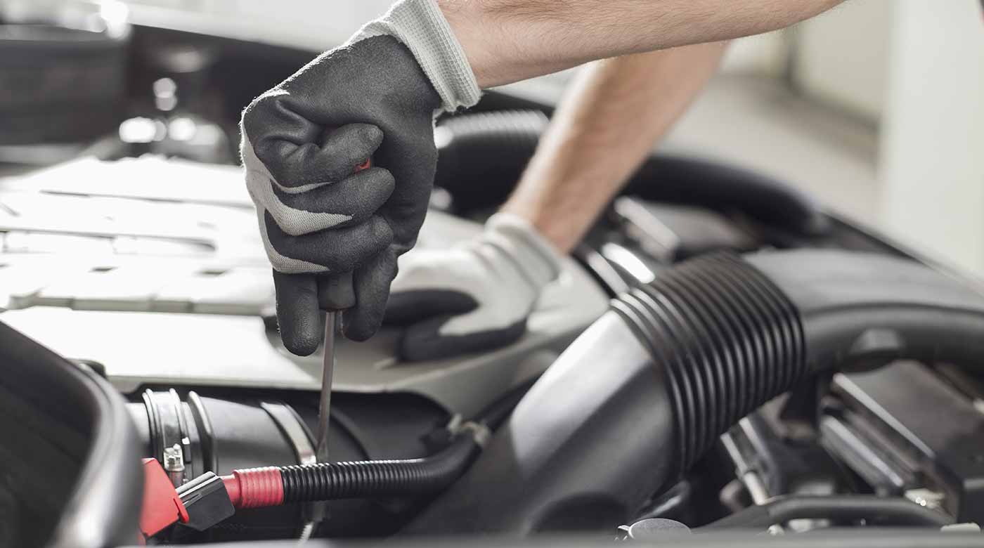 Mechanikerhände mit Handschuhen arbeiten mit Werkzeug am Motor eines Fahrzeugs.