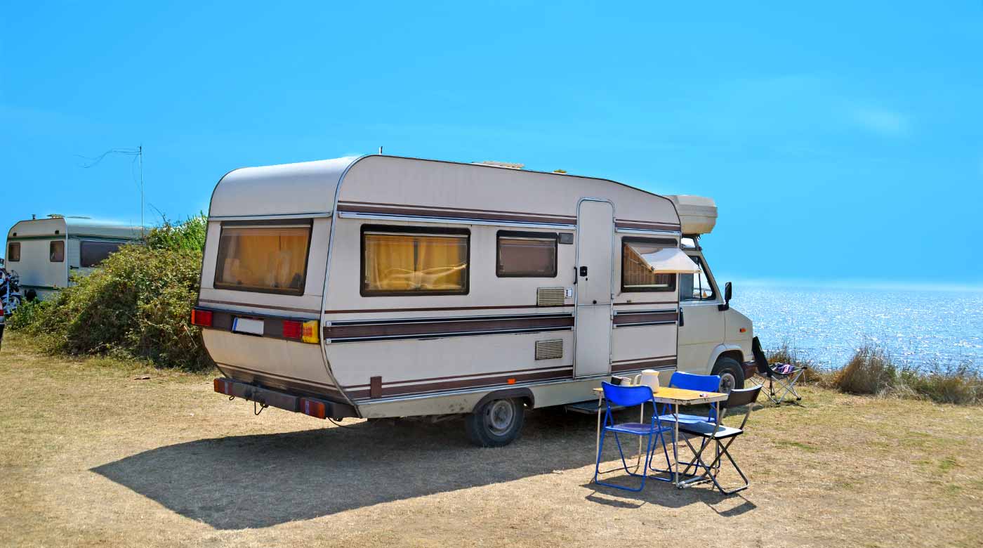 Wohnmobil steht auf einem Campingplatz am Meer mit Tisch und Stühlen im Vordergrund.