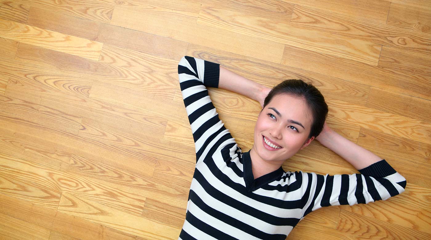 Person entspannt auf hellem Holzfußboden, trägt gestreiftes Oberteil.