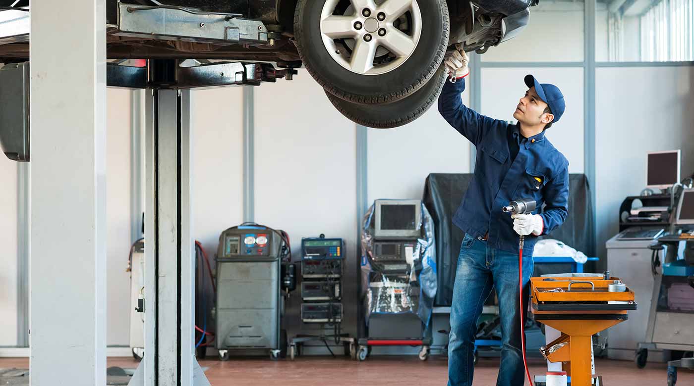 Mechaniker arbeitet mit Werkzeug an einem angehobenen Auto in einer Werkstatt.