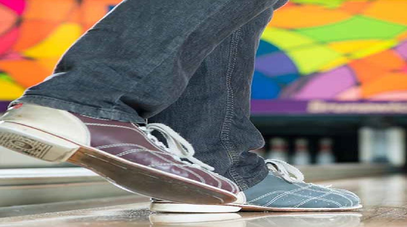 Nahaufnahme von Bowling-Schuhen auf der Bahn, bunte Wand im Hintergrund.