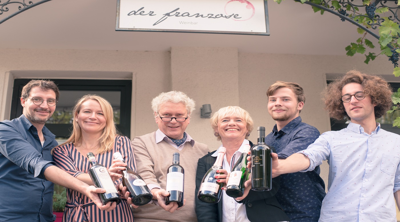 Sechs Personen vor Weinbar „der franzose“ präsentieren verschiedene Weinflaschen.